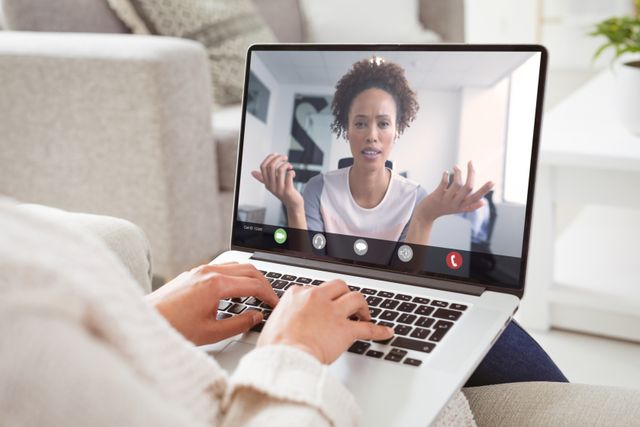Image shows a Caucasian woman arm using a laptop in a comfortable home environment for a video conference with an African American female colleague. Ideal for illustrating remote work, virtual communication, modern technology in business, and teamwork in the digital age.