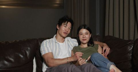 Couple cuddling on leather sofa sharing quiet conversation and snacks in cozy living room