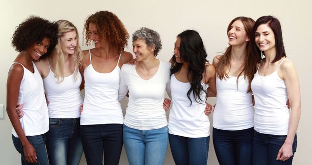 Group of diverse women standing together wearing white tops and jeans, smiling and bonding. Perfect for illustrating themes of diversity, friendship, and unity. Suitable for promoting women's groups, equality campaigns, and fashion collections. Ideal for use in marketing materials, social media campaigns, and lifestyle blogs.