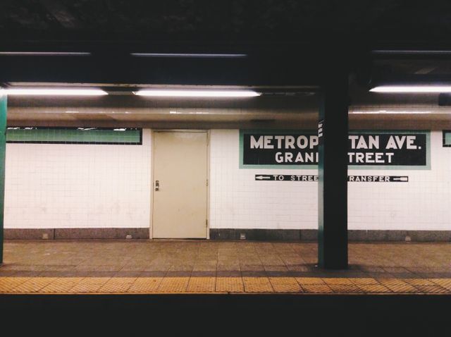 This photo shows a deserted subway station platform with clear signage for Metropolitan Ave Grand Street. Suitable for use in urban lifestyle blogs, travel websites, articles on city transportation systems, or any content related to public commuting. Ideal for presentations discussing urban planning or public transit infrastructure.