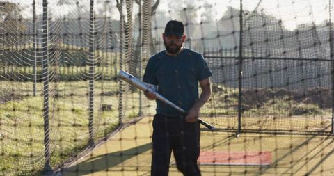 Mature man practicing batting in outdoor batting cage with net shadows and sunlight