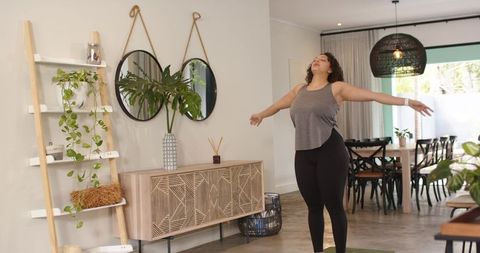 African american woman stretching on yoga mat in bright bohemian living and dining space