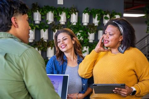 Diverse team collaborating at modern workspace with laptop and tablet by plant wall