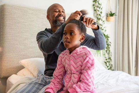 African american father brushing daughter hair on bed morning family bonding