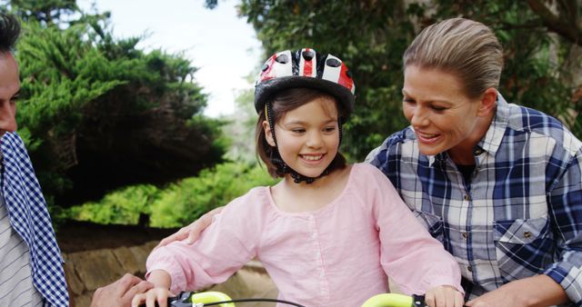Parents teaching daughter to ride a bicycle in a park, emphasizing support and togetherness. Ideal for promoting family activities, parenting advice, and outdoor recreation.