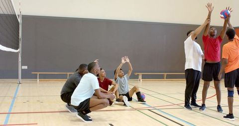 Diverse male volleyball team practicing blocking and teamwork drills in indoor gymnasium