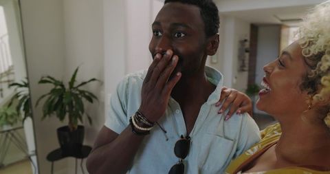 Couple celebrating new home with surprised reaction in sunlit entryway, welcoming moment