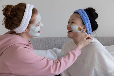 Caucasian and asian friends applying mint face mask during cozy at-home spa night