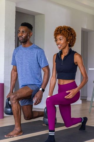 African american couple performing kettlebell lunges in bright home workout studio