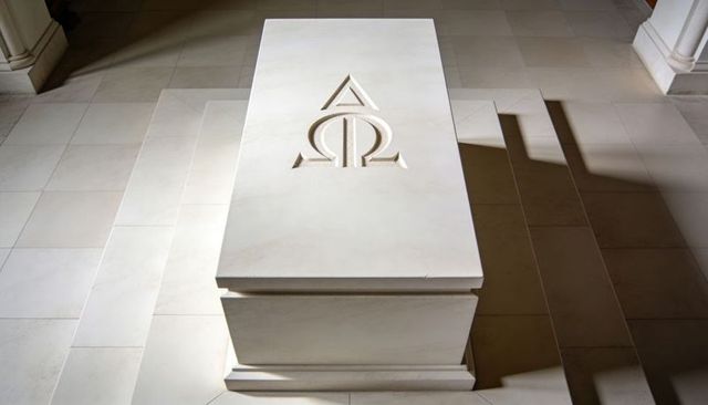 Sunlit marble tomb featuring alpha omega carving on minimalist mausoleum plinth