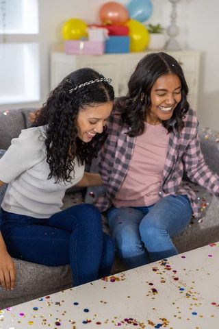 Multicultural friends celebrating with confetti on couch, laughing at birthday party