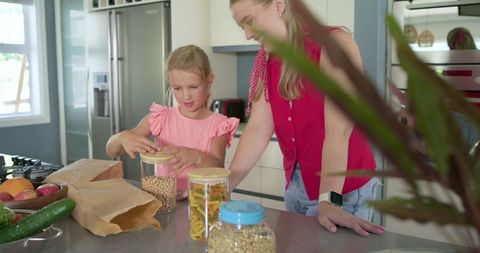 Mother and daughter organizing pantry jars in modern kitchen teaching healthy habits