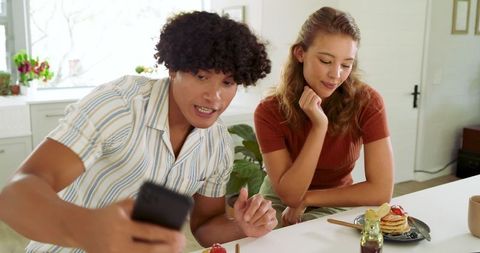 Diverse Couple Enjoying Breakfast and Taking Selfies in Modern Kitchen