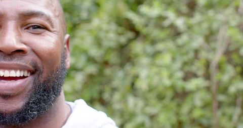 African american mature man smiling in garden wearing hoodie with green bokeh