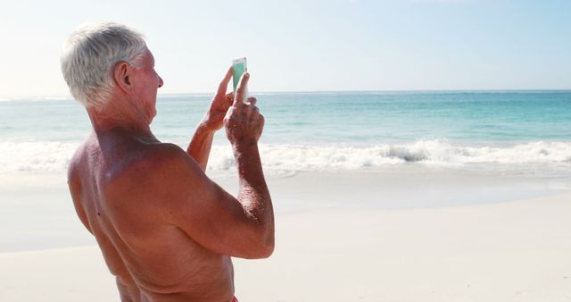 Retired old man standing while taking pictures on the beach - Download Free Stock Photos Pikwizard.com