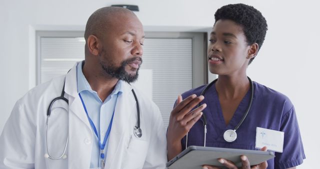 African american male and female doctors using tablet, talking at hospital. Medicine, healthcare, lifestyle and hospital concept.