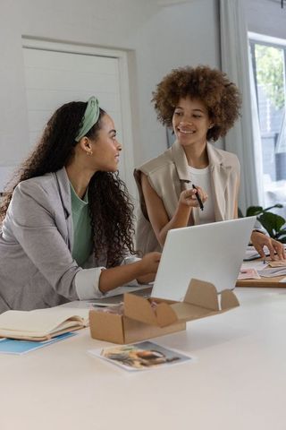 African american women collaborating over laptop and product samples in bright studio