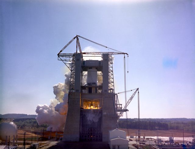 This photograph depicts a dramatic view of the first test firing of all five F-1 engines for the Saturn V S-IC stage at the Marshall Space Flight Center. The testing lasted a full duration of 6.5 seconds. It also marked the first test performed in the new S-IC static test stand and the first test using the new control blockhouse. The S-IC stage is the first stage, or booster, of a 364-foot long rocket that ultimately took astronauts to the Moon. Operating at maximum power, all five of the engines produced 7,500,000 pounds of thrust. Required to hold down the brute force of a 7,500,000-pound thrust, the S-IC static test stand was designed and constructed with the strength of hundreds of tons of steel and cement, planted down to bedrock 40 feet below ground level. The structure was topped by a crane with a 135-foot boom. With the boom in the up position, the stand was given an overall height of 405 feet, placing it among the highest structures in Alabama at the time. When the Saturn V S-IC first stage was placed upright in the stand , the five F-1 engine nozzles pointed downward on a 1,900 ton, water-cooled deflector. To prevent melting damage, water was sprayed through small holes in the deflector at the rate 320,000 gallons per minute. 