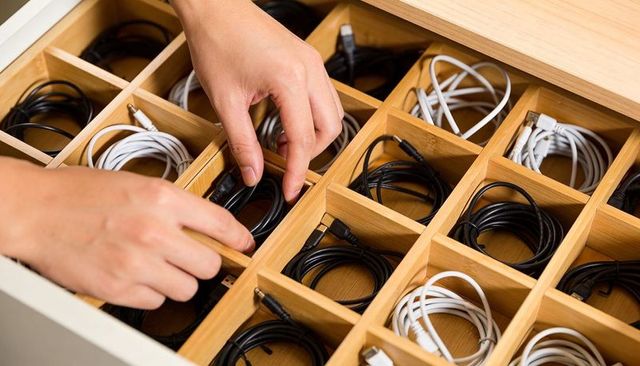 Hands organizing usb-c and 3.5mm cables in bamboo compartment drawer for neat cable storage