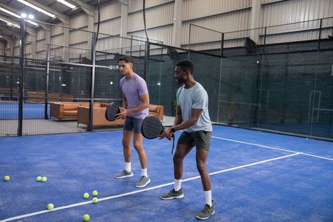 Diverse male friends practicing padel holding rackets on indoor blue court