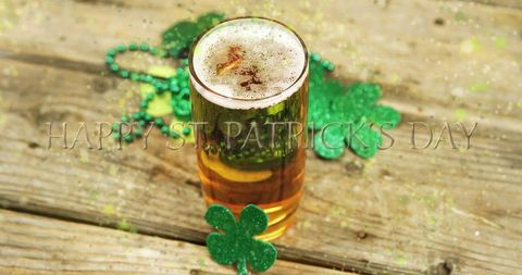 Toasting amber beer with glitter shamrocks celebrating st patricks day on rustic wood