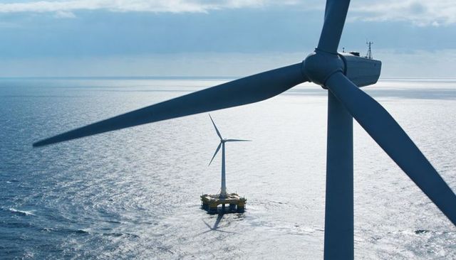 Offshore wind turbine dominating foreground with floating platform shadow above sea horizon