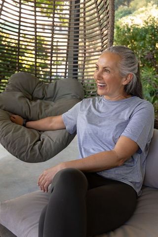 Senior woman relaxing in rattan hanging chair on patio smiling and checking wristband