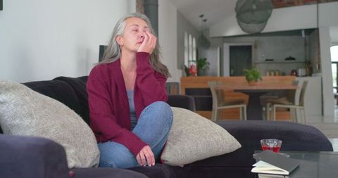 Senior woman rubbing eye on sofa in cozy open-plan living room