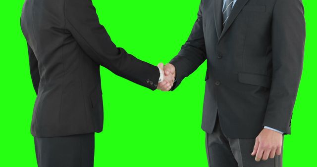 Two businessmen are shaking hands in a gesture of agreement or partnership, with copy space on a green background. Their professional attire suggests a formal business setting or transaction.