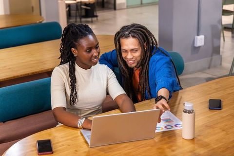 African American coworkers collaborating on laptop reviewing charts in modern coworking hub