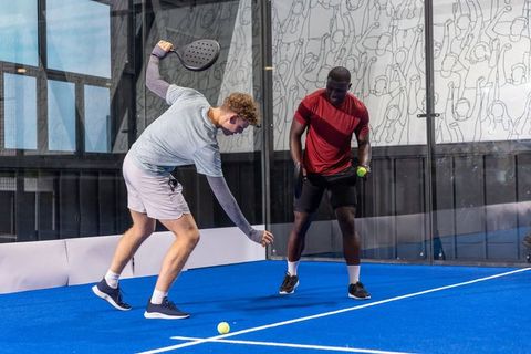 Two diverse male players playing padel on bright blue court rallying with paddles and ball