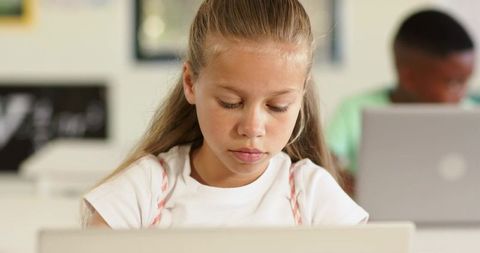 Young Girl Concentrating on Laptop in Bright Classroom Learning Environment