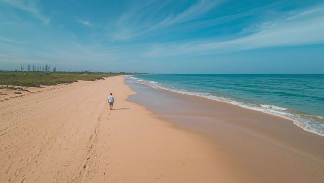 Walking lone figure along empty sandy beach with footprints and turquoise ocean horizon