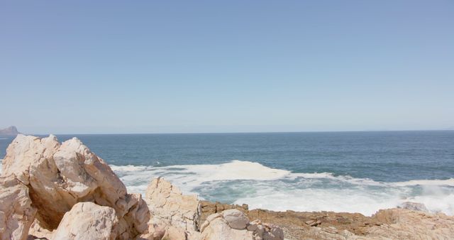 The image depicts a serene ocean view with gentle waves crashing against rocky shoreline under a clear sky. This scene is ideal for projects related to nature, travel, and relaxation, such as websites promoting coastal tourism, wellness retreats, wallpapers, and backgrounds conveying calmness and beauty of seaside destinations.