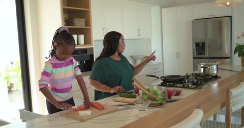 African american mother and daughter chopping vegetables together in modern bright kitchen