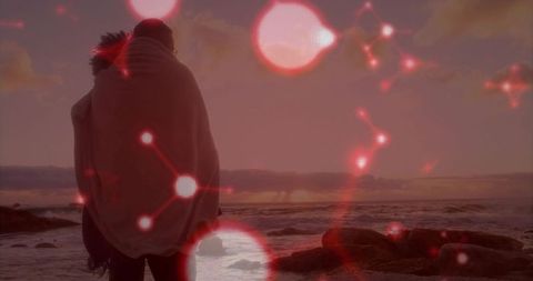 Silhouetted couple wrapped in blanket at sunset on rocky shore with red network overlay