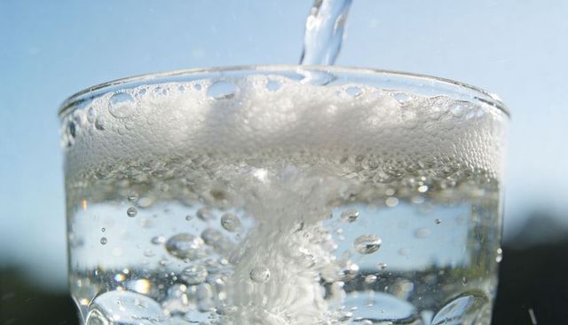 Pouring sparkling water into clear glass with rising bubbles and foam in sunlight