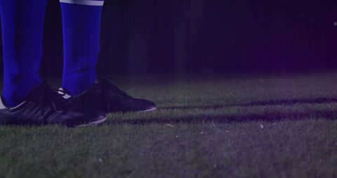 Soccer Player Stands on Grass with Blue Socks at Night in Stadium