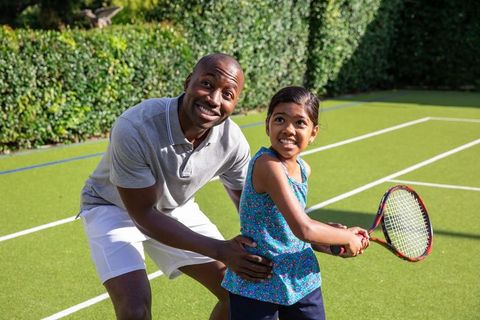 Father Teaching Daughter Tennis on Sunny Synthetic Court