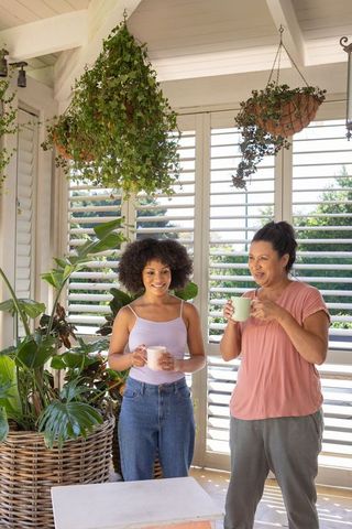 Mother and Daughter Relaxing in Sunroom Surrounded by Hanging Plants