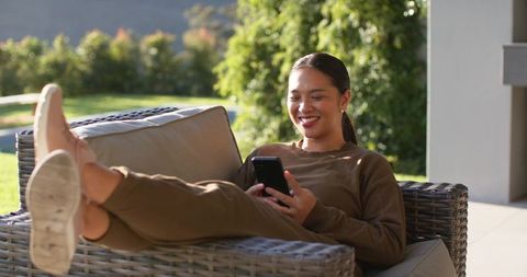 Young Woman Relaxing on Outdoor Patio Sofa with Smartphone