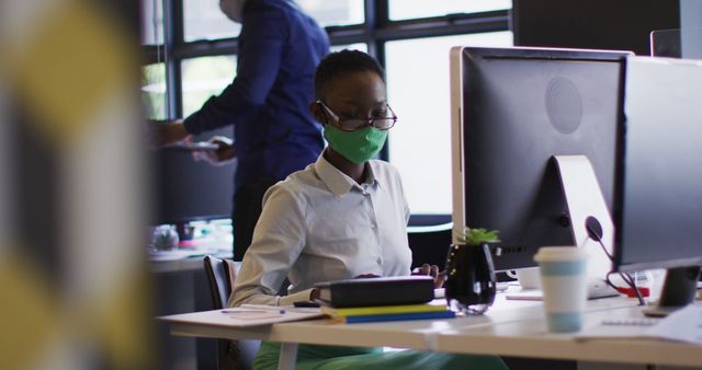 Young professional woman wearing mask working at desk in modern office - Download Free Stock Images Pikwizard.com