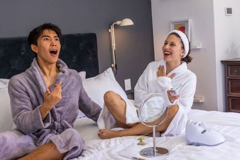Diverse couple enjoying at-home spa night testing skincare gadgets and led mask
