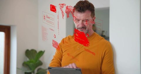 Mature man interacting with tablet and red holographic interface in minimal home corner
