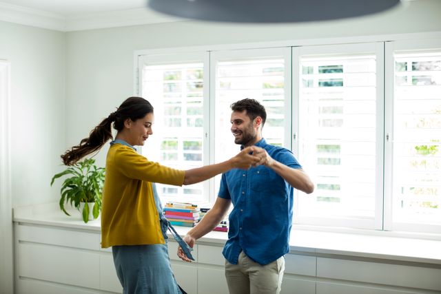 This image captures a joyful moment of a couple dancing together in their kitchen. They are smiling and enjoying each other's company, showcasing a strong bond and love. This image can be used for advertisements, blogs, or articles related to relationships, home life, happiness, and leisure activities.