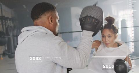Trainer holding focus mitt guiding female boxer throwing punch in boxing ring workout