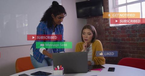 Female colleagues collaborating on laptop with social notifications in office