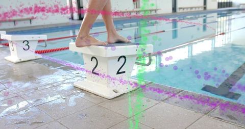Standing swimmer adjusting stance on block 2 at indoor pool with paint splatter competition