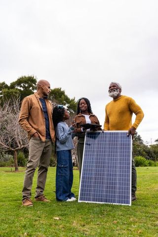 Multigenerational african american family holding solar panel and tablet on lawn