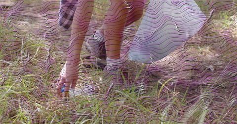 Kneeling woman reaching into grassy meadow touching soil near lavender skirt and white slip-ons